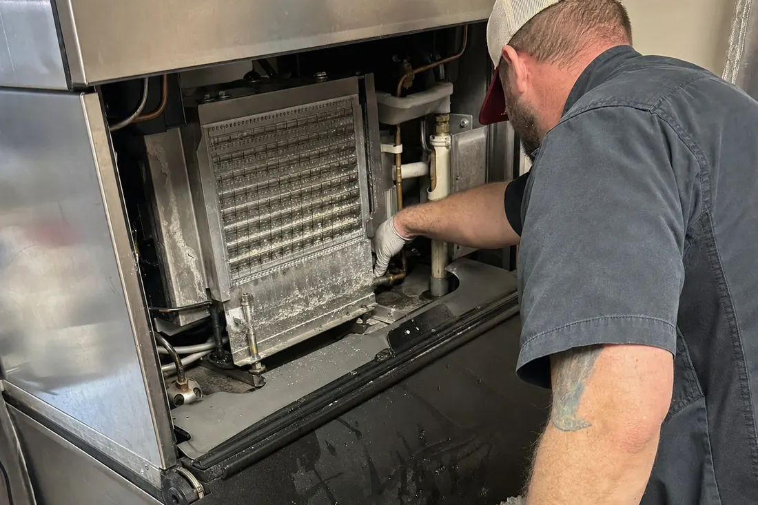 Technician at a stainless ice machine with the top panel off, checking the water line and the evaporator plate, the evaporator plate visible in the picture - Terms of use