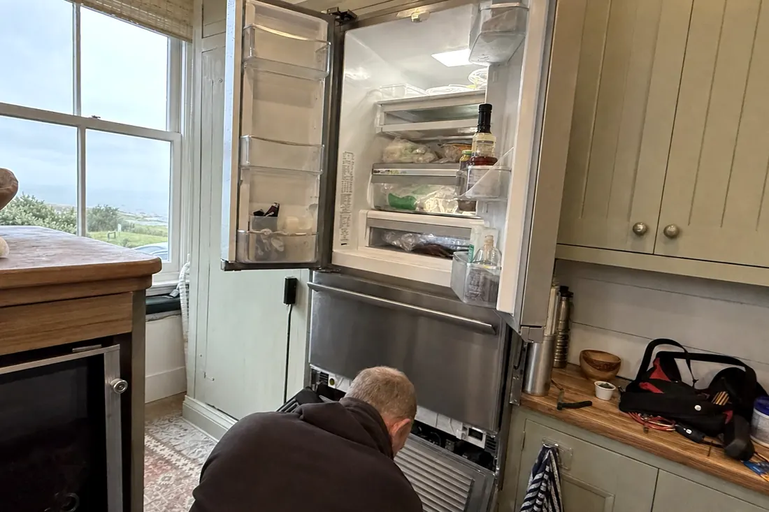 An open built-in refrigerator in a coastal kitchen, technician at the lower grille, the interior shelves in frame - Appliance repair in Ponte Vedra Beach and Nocatee