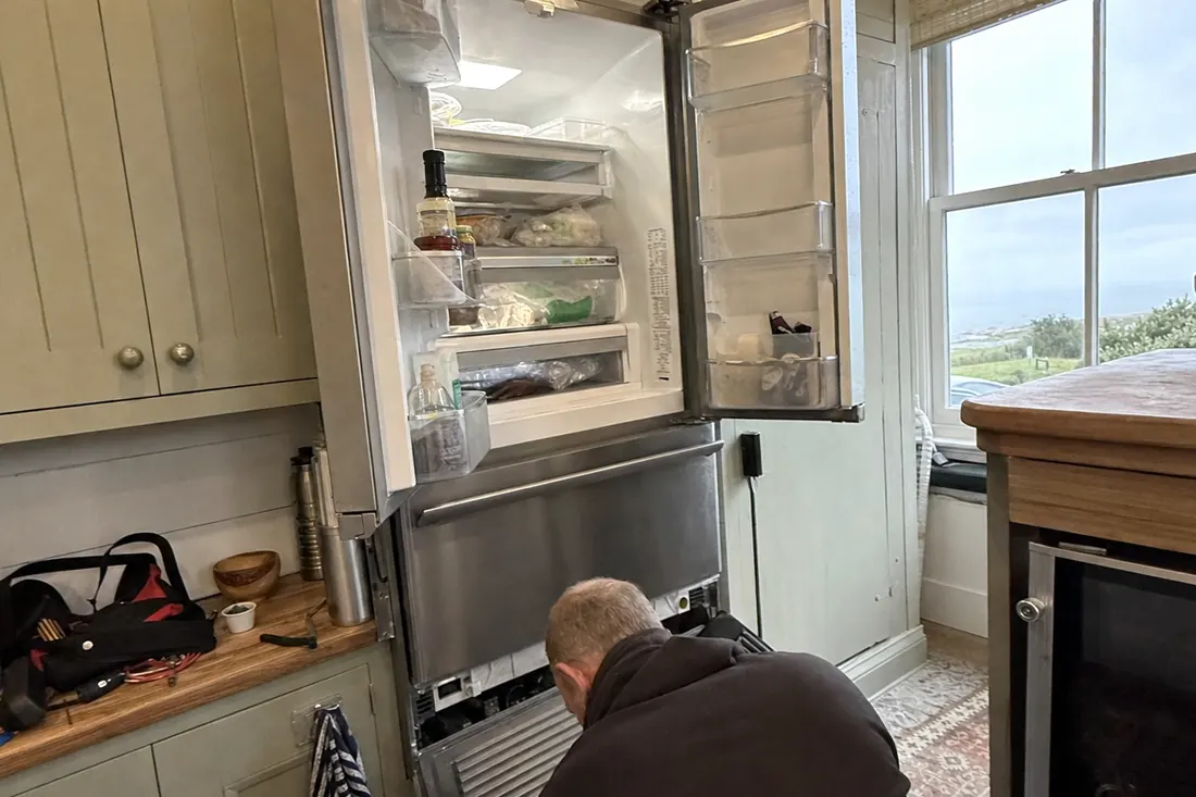 An open built-in refrigerator in a coastal kitchen, technician at the lower grille, the open doors visible in the picture - Salt air and coastal appliance corrosion