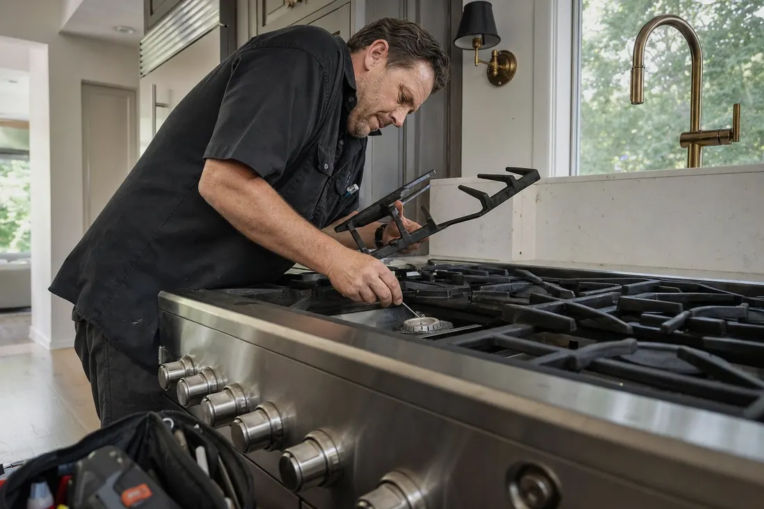 Technician checking a sealed burner on a professional gas range, one grate lifted - Brands we service
